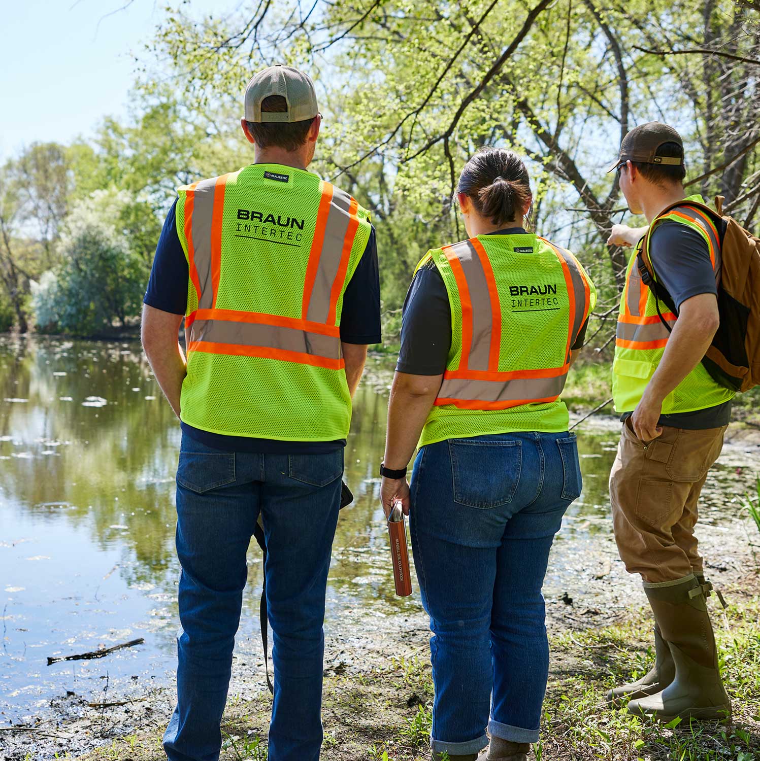 Three workers in safety vests standing near a pond