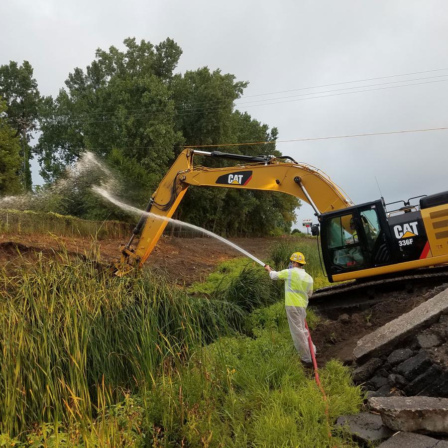 Man with PPE on, spraying water near an excavator